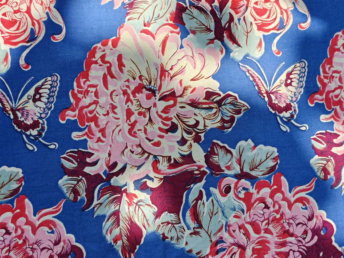Blue-ground multicolour printed cotton with large pink flower clusters and naturalistic butterflies.