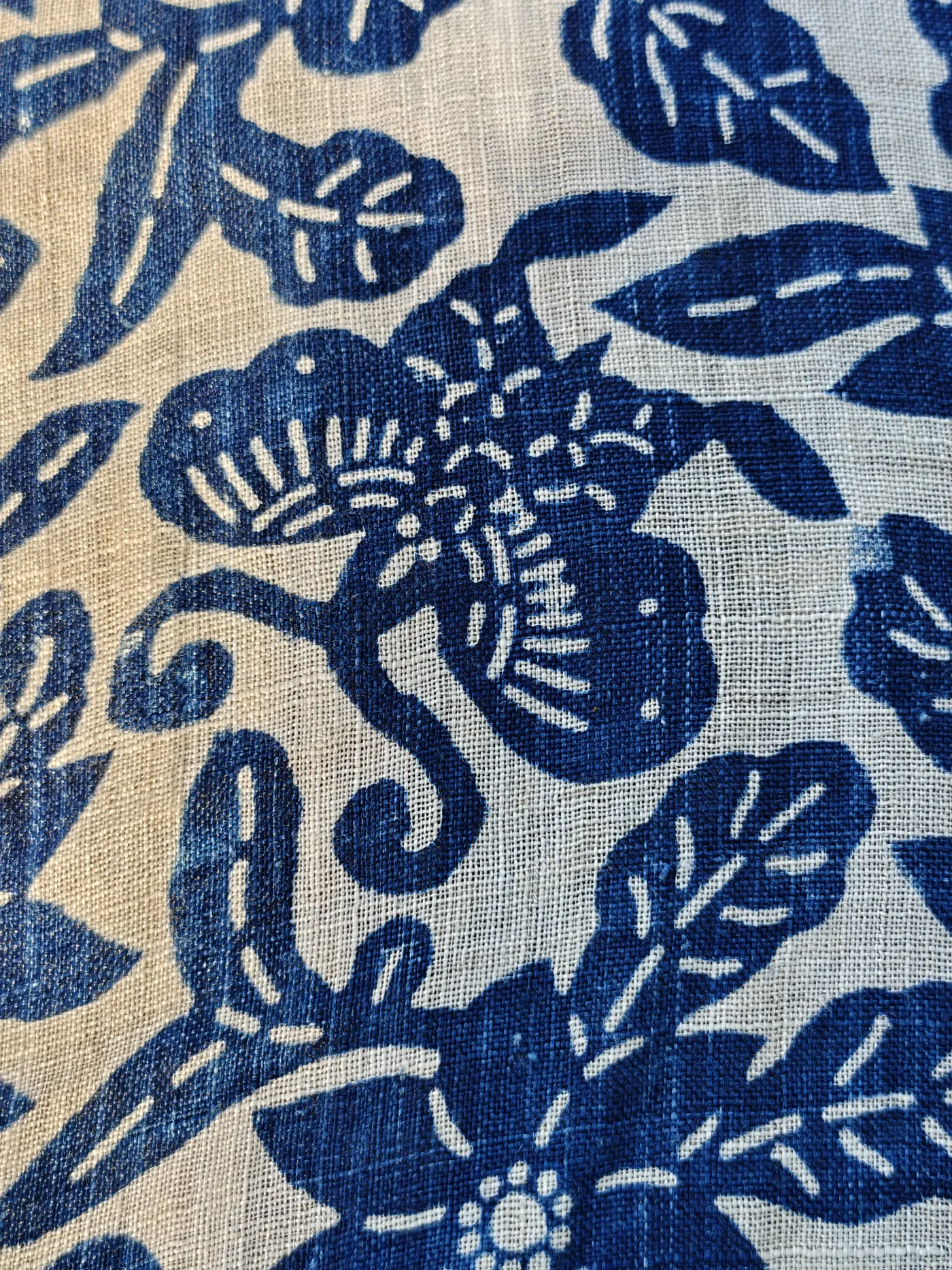 Close detail of a blue-and-white resist-style butterfly surrounded by leaves and flowers on an open woven ground.