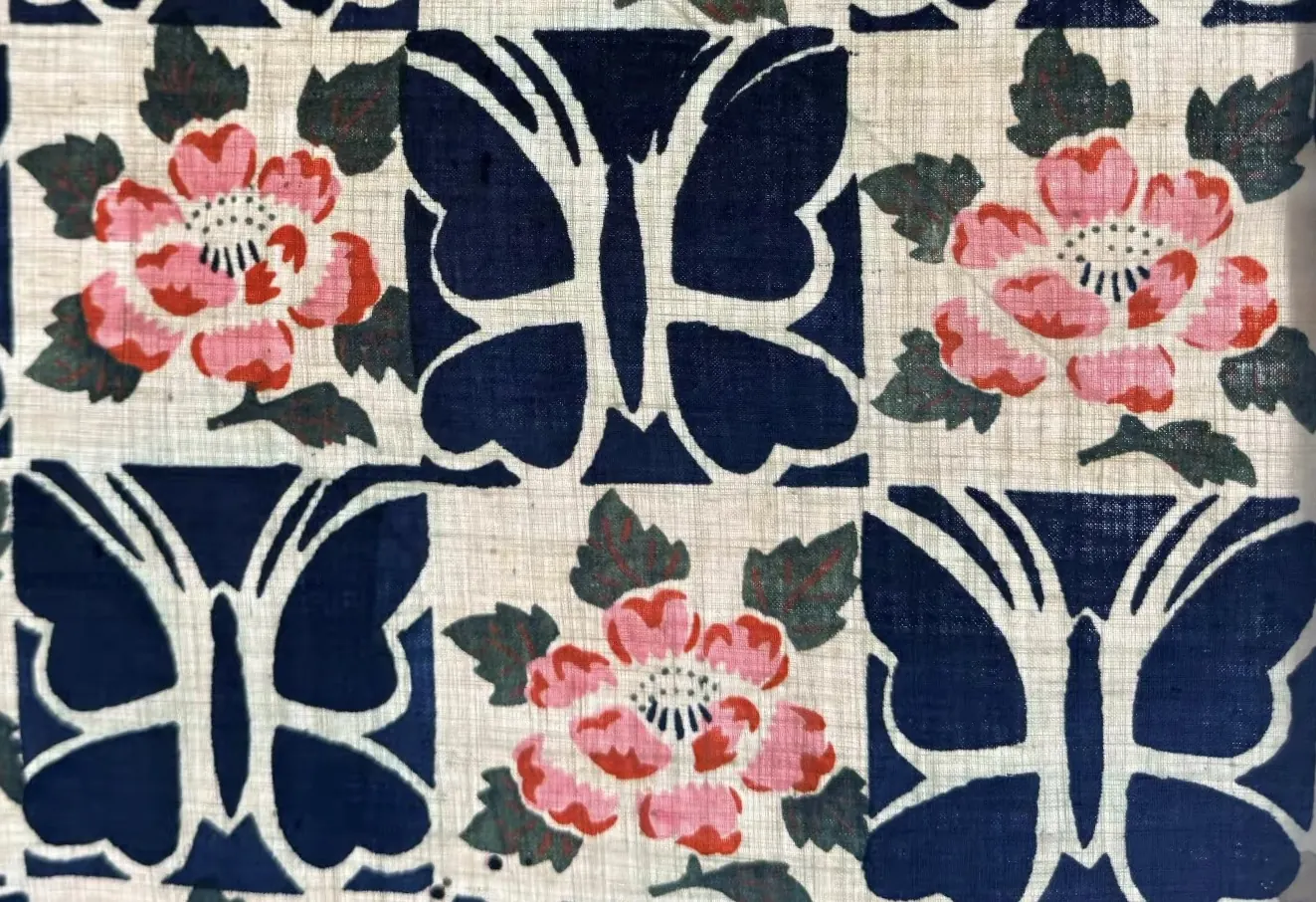 Large dark-blue graphic butterflies alternating with pink flowers across a pale printed textile.