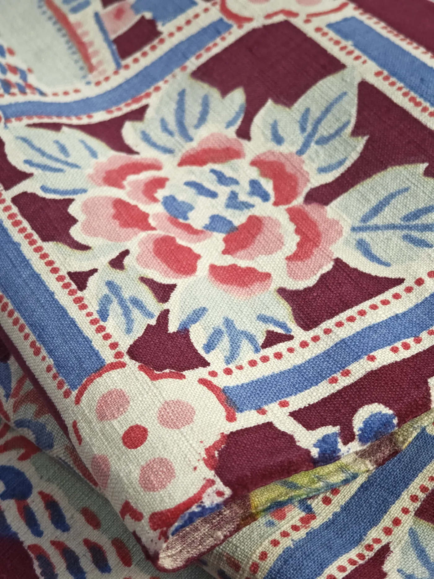 Close-up of a pink peony on a burgundy, blue and pale green printed textile.