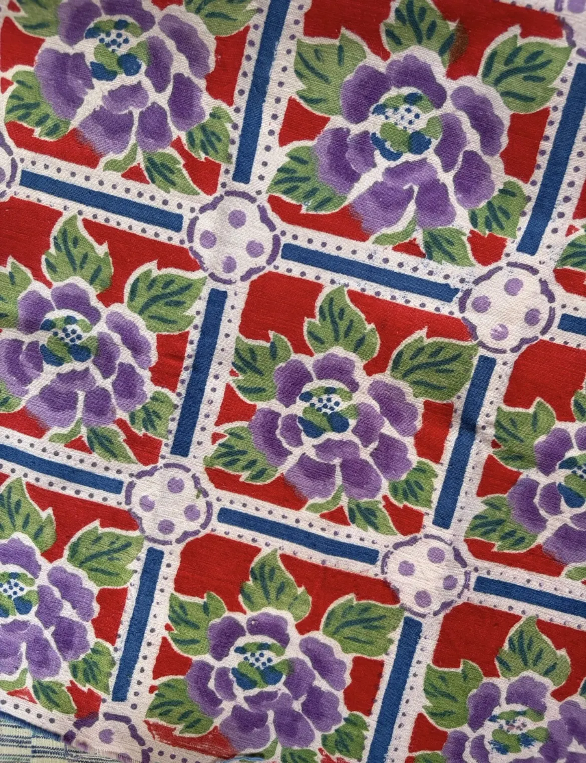 Wider repeat of purple peonies in red panels separated by blue bars and dotted roundels.